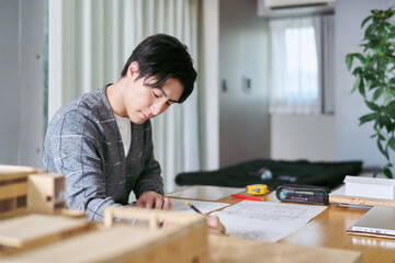 自宅兼事務所で建築模型の置かれたテーブルで印刷された図面のチェックと修正をする建築士の男性