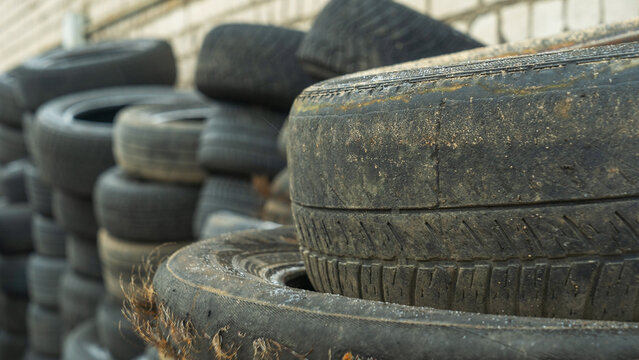 Close-up view of discarded old car tires outdoors, showcasing a pile of used tires ready for recycling. Highlighting environmental concerns and rubber waste management. Defocused background.