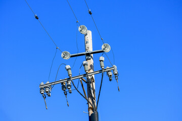 Electrical utility wooden pole with multiple insulators, wires and power lines against a vibrant blue sky
