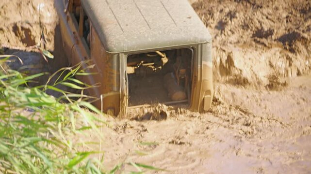 The SUV tries to drive through a muddy puddle and gets stuck on a challenging clay hill. The car is covered in mud. Because of the missing fifth door, the interior of the SUV can be seen. Slow motion