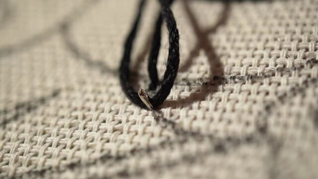 Children's crafts. Embroidering with black floss threads on canvas. A girl learns to embroider. Close-up of a needle with thread used for embroidering.