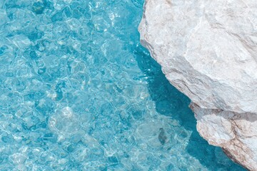 A serene view of clear blue water beside a textured rock.