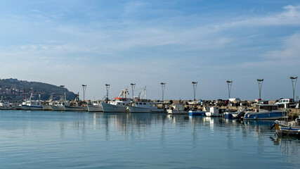 Fototapeta premium Peaceful seaside marina with docked fishing boats, reflecting calm coastal life, perfect for summer getaways