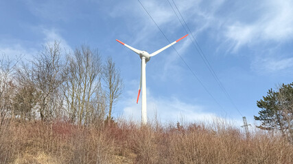Fototapeta premium Wind turbine on a hill under a blue sky, renewable energy, sustainability, eco-friendly technology