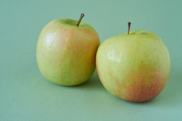 Two ripe green and red apples on a green background, close-up