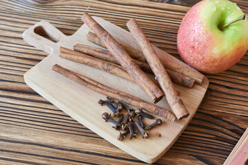 Cinnamon sticks and an apple on a cutting board on a wooden background