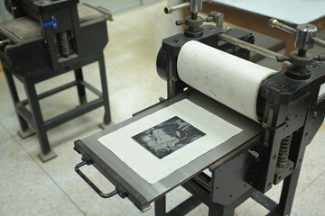 An inked artwork on an Intaglio printing plate is lying on the press bed of the etching press...