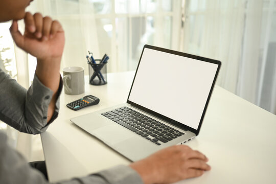 A close-up of a professional businessman sits at a desk, staring at a blank laptop screen. A calculator, pen holder, and coffee mug are nearby