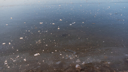 Delicate ice forms on the lake's surface as spring arrives, showcasing intricate patterns of melting. This serene scene captures the beauty of nature's transition from winter to spring.