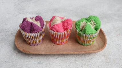 Colorful Bolu Kukus (Sponge Cake), made from flour, tapioca flour, egg and sugar. Served on wooden plate isolated on grey background. Indonesian traditional snack