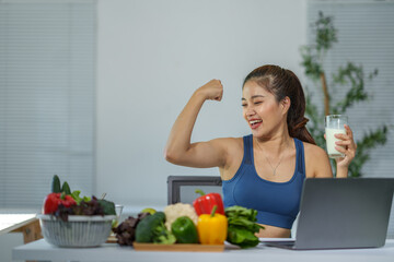 Young athletic woman flexing her biceps while drinking a glass of milk and eating healthy food, promoting a fit and healthy lifestyle with a balanced diet and regular exercise