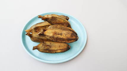 Pisang Kukus or Steamed Banana, Indonesian traditional food, served on blue round plate. isolated on grey background