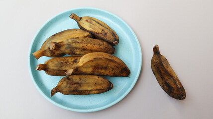 Pisang Kukus or Steamed Banana, Indonesian traditional food, served on blue round plate. isolated on grey background
