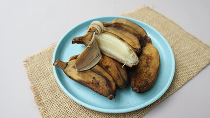 Pisang Kukus or Steamed Banana, Indonesian traditional food, served on blue round plate. isolated on grey background