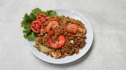 Nasi goreng- Indonesian fried rice with shrimp, tomato and vegetables in white plate on grey background. Indonesian Food