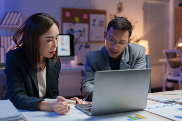 Two business professionals engage in a collaborative discussion, analyzing data on a laptop in a modern office setting. Charts and notes are visible, emphasizing teamwork and strategy