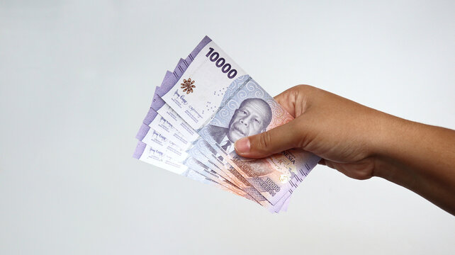 Closeup of a hand of an Asian woman with brown skin holds a 10,000 rupiah banknote from Indonesia isolated on white background