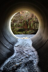View through a round concrete tunnel carrying a stream beneath a road