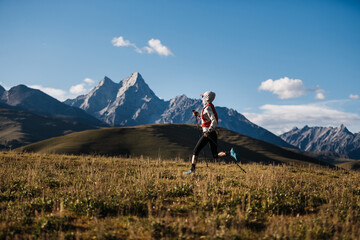 Fototapeta premium Woman trail runner running on grassland with rocky mountains in the distance