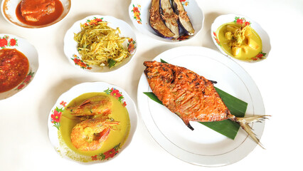 Various menus on white plates from a Padang cuisine restaurant consisting of fish grilled, eggplant, pawn curry arranged in neat pile table. Minang or Minangkabau food.