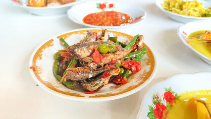 Various menus on white plates from a Padang cuisine restaurant consisting of fried small fish with red chilli arranged in neat pile table. Minang or Minangkabau food.