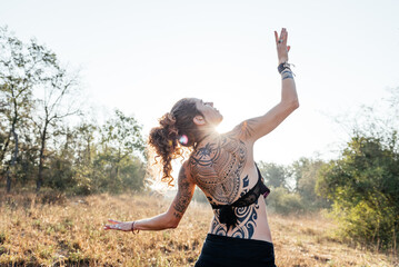 Tribal Dancer Poses With Tattooed Back Against Sunlight in Natural Setting
