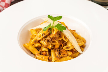 Top view of penne bolognese pasta in white plate on wooden table