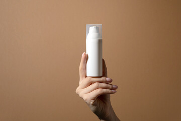 Female hand holding plastic unbranded tube. Flacon for cream, body lotion, toiletry. Container for professional cosmetics product. Mockup, copy space. Isolated Brown background with copy space
