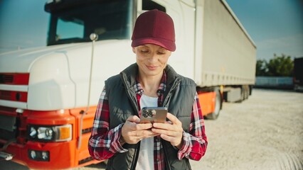 Beautiful Caucasian woman standing next to her truck while using mobile phone. Typing on screen with fingers. Browsing social media or texting with friends online. Socializing remotely.