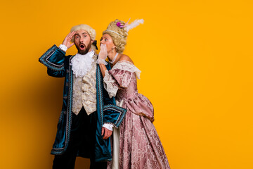 Playful couple in elegant historical costumes posing against a vibrant yellow background at a themed event