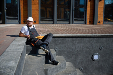 Construction worker relaxing near empty swimming pool. Builder in uniform has a break sitting in...