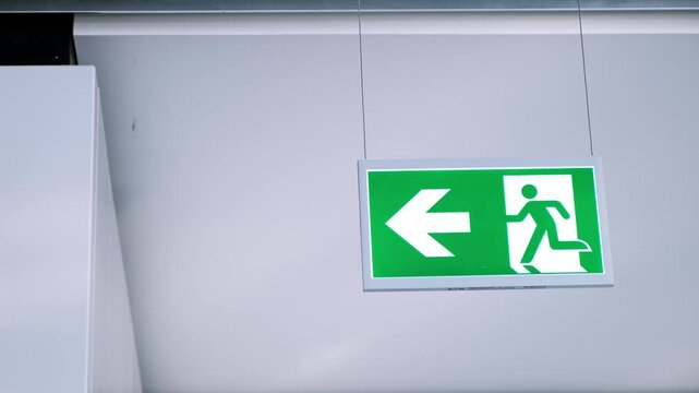 Emergency exit sign. The left arrow direction of movement in case of fire in building. Illuminated plexiglass icon. Symbol of running person. Glass material. Copy space. High quality 4k footage.