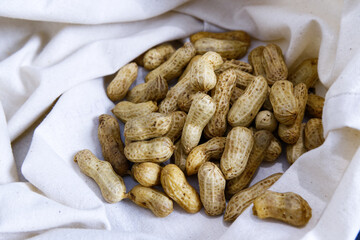 Boiled peanuts on a calico bag. Close-up a group of peanuts for eating. Organic food for eating healthy, vegan snacks, fiber, beige fabric texture, and homemade boiled food concepts.