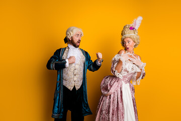 Fototapeta premium Joyful couple in vintage costumes portraying royalty against a vibrant yellow backdrop, showcasing historic charm and cosplay creativity