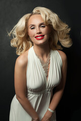 Naklejka premium Attractive blond woman with makeup and perfect wavy hair posing on black studio wall background, portrait