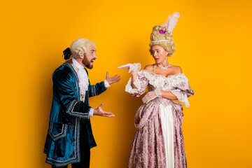 Fototapeta premium Elegant couple in historical costumes posing playfully against a vibrant yellow backdrop