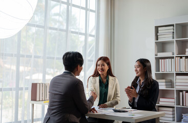 Three business professionals engage in a productive meeting, exchanging ideas and shaking hands in a bright office space with large windows and shelves filled with books
