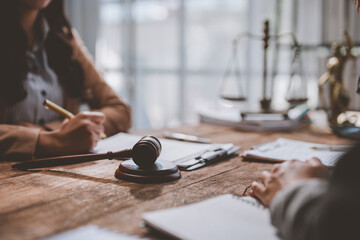 Two legal professionals collaborate at a wooden desk, discussing documents and strategies. A gavel and scales of justice symbolize the legal environment and decision-making process