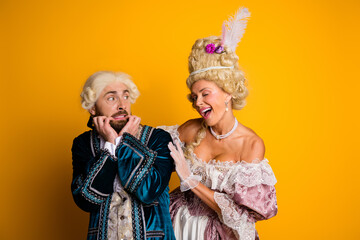 Elegant couple dressed in vintage period costumes posing with humor and grace on vibrant yellow backdrop