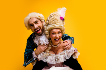 Playful couple in historical costumes enjoying their time posing with cheerful expressions, set against a vibrant yellow background