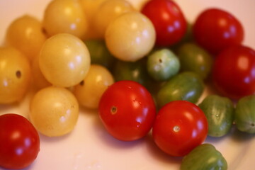 A selection of colorful tomatoes arranged on a white plate for display or use in various recipes.