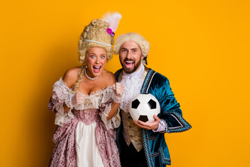 Cheerful couple dressed in royal costumes celebrating fun moment with soccer ball on vibrant yellow background