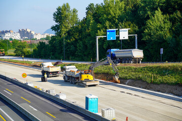 Naklejka premium Excavator and Dump Trucks Working on Highway Shoulder, Moving Earth Materials