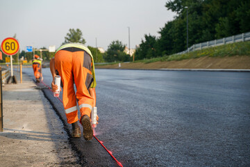 Construction Worker Marking Fresh Asphalt with Spray Can on Highway