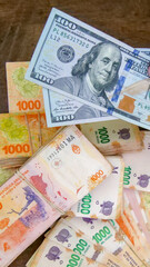 Vertical image of two 100 American dollar bills and  many 1000 Argentine peso bills, signifying the exchange rate, dollar blue, and hyperinflation economic situation currently in Argentina