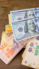 Vertical image of two 100 American dollar bills and  many 1000 Argentine peso bills, signifying the...