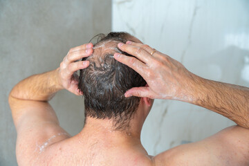 Naklejka premium man soaps his head in the shower, head with a bald spot, standing with his back to the camera, close-up shot. High quality 4k footage