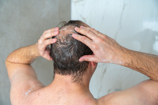 man soaps his head in the shower, head with a bald spot, standing with his back to the camera, close-up shot. High quality 4k footage