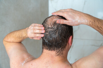 Naklejka premium man soaps his head in the shower, head with a bald spot, standing with his back to the camera, close-up shot. High quality 4k footage