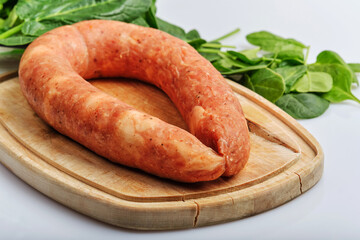 A ring of homemade chicken sausage lies on a cutting board surrounded by spinach leaves
